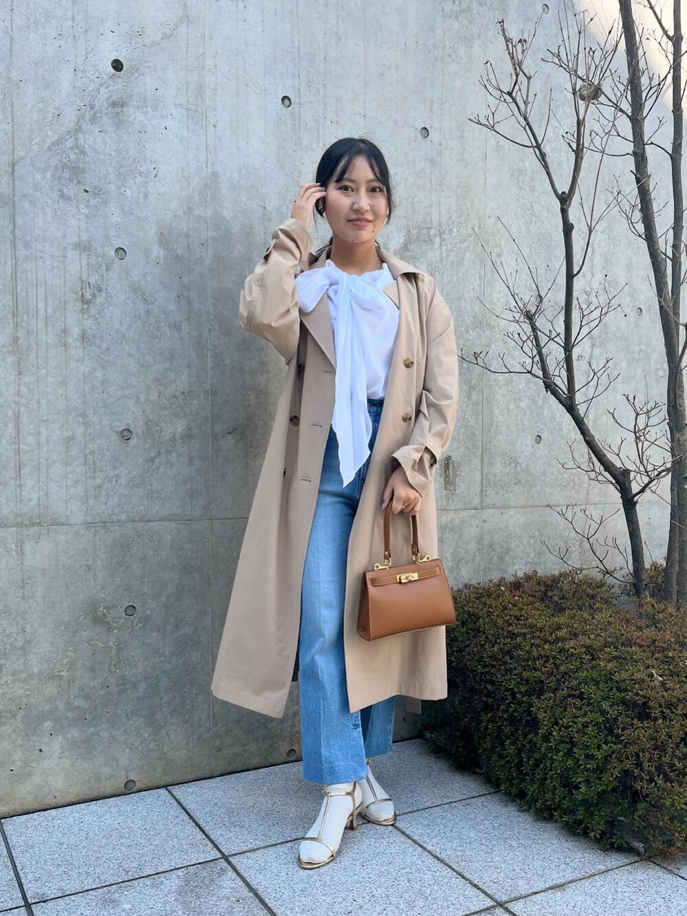 ホワイト系のシャツ/ブラウス、ベージュ系のトレンチコート、ブルー系のデニムパンツを着用したレディースの春コーディネートの2枚目の写真