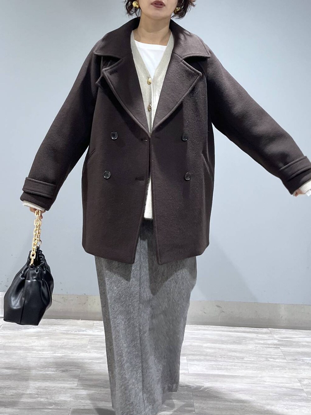 ブラウン系のピーコート、ホワイト系のカーディガン/ボレロ、ブラック系のブーツを着用したレディースの秋コーディネートの6枚目の写真