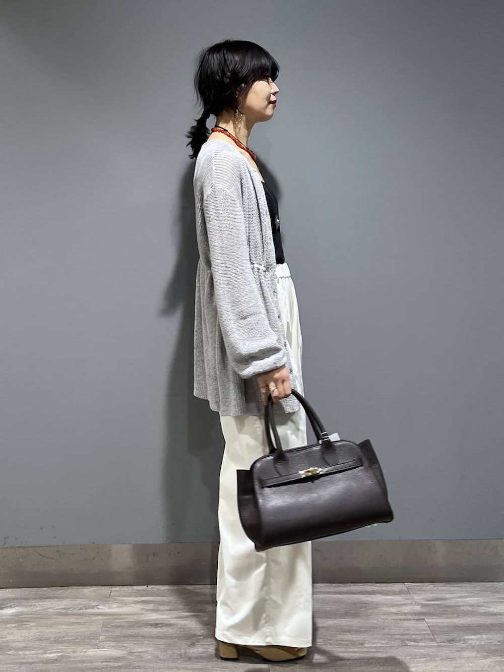 ブラウン系のショルダーバッグ、ホワイト系のスラックス、グレー系のカーディガン/ボレロを着用したレディースの春コーディネートの2枚目の写真