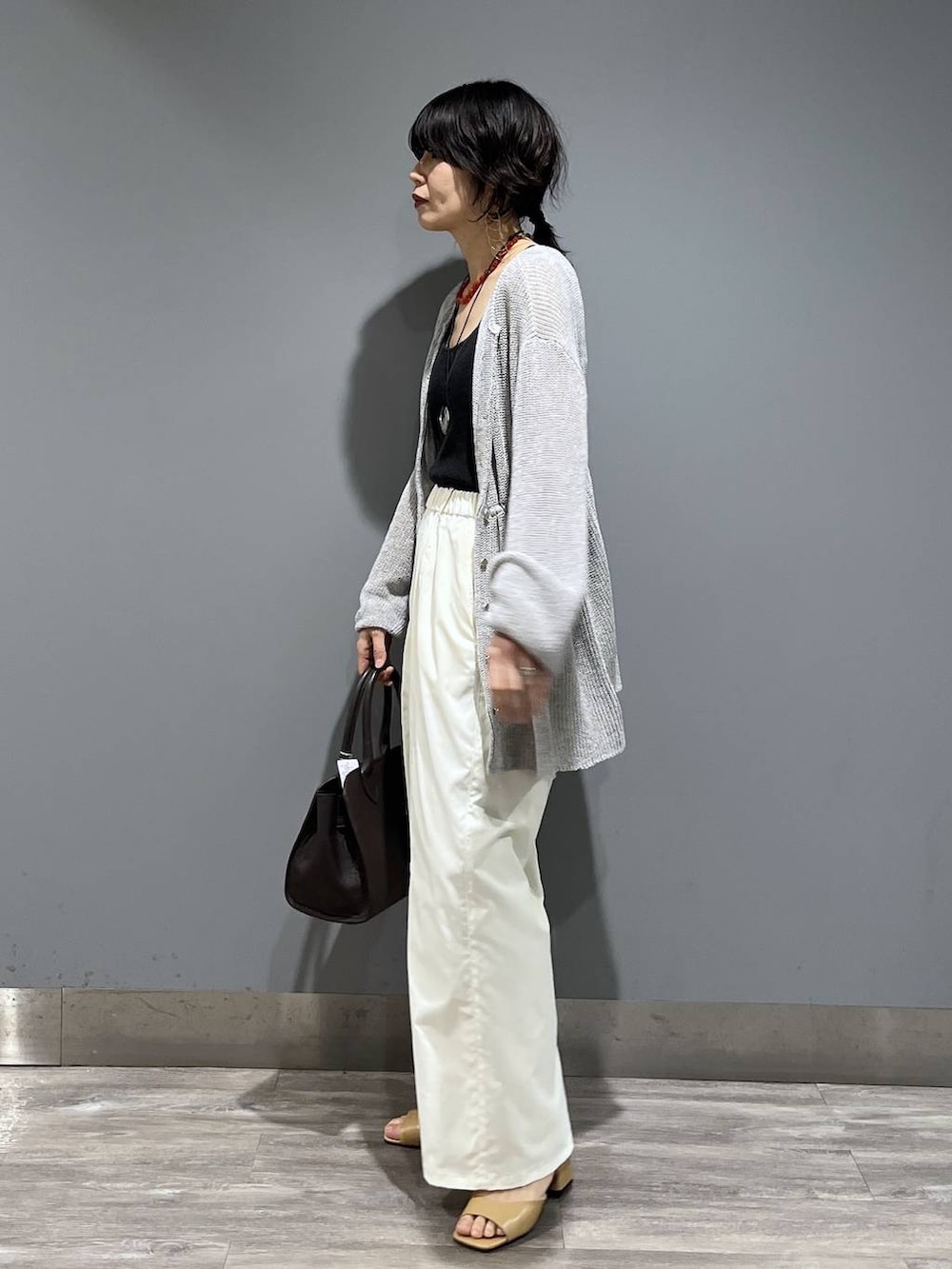ブラウン系のショルダーバッグ、ホワイト系のスラックス、グレー系のカーディガン/ボレロを着用したレディースの春コーディネートの5枚目の写真
