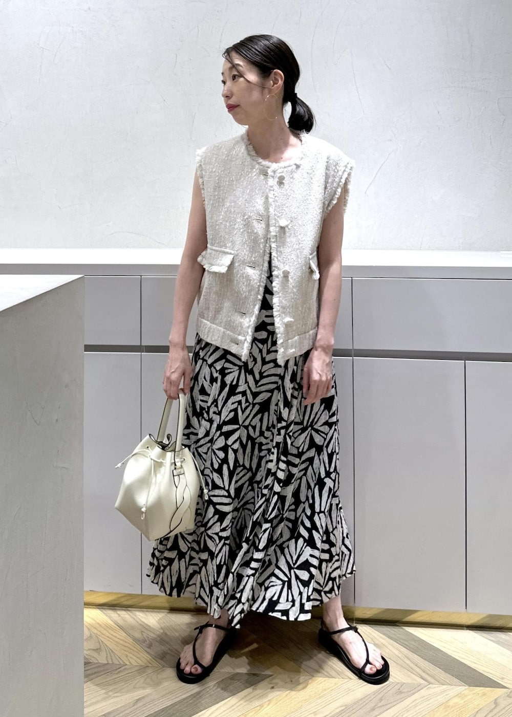 ホワイト系のショルダーバッグ、ブラック系のサンダル、ホワイト系のベストを着用したレディースの夏コーディネートの2枚目の写真