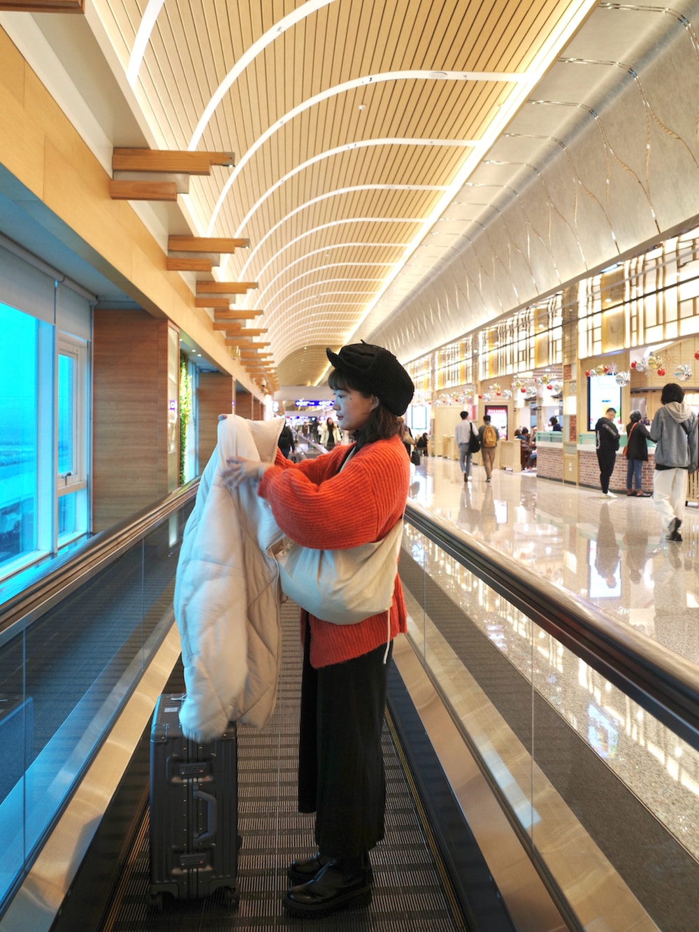 オレンジ系のカーディガン/ボレロ、ホワイト系のダウンジャケット/コート、ブラック系のブーツを着用したレディースの冬コーディネートの2枚目の写真