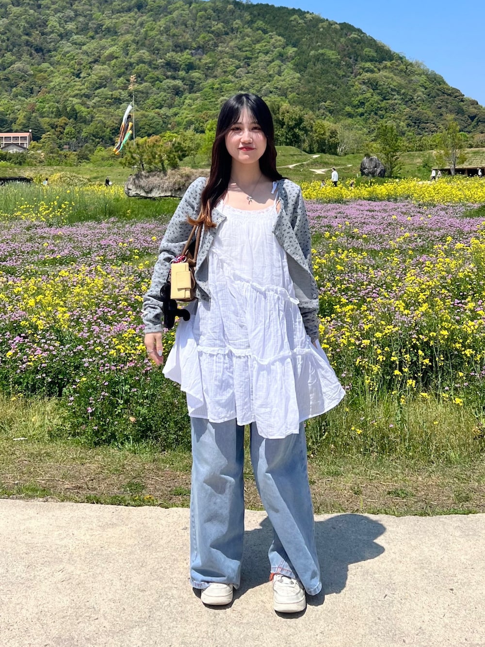 ブルー系のデニムパンツ、グレー系のカーディガン/ボレロ、ホワイト系のチュニックを着用したレディースの春コーディネートの2枚目の写真