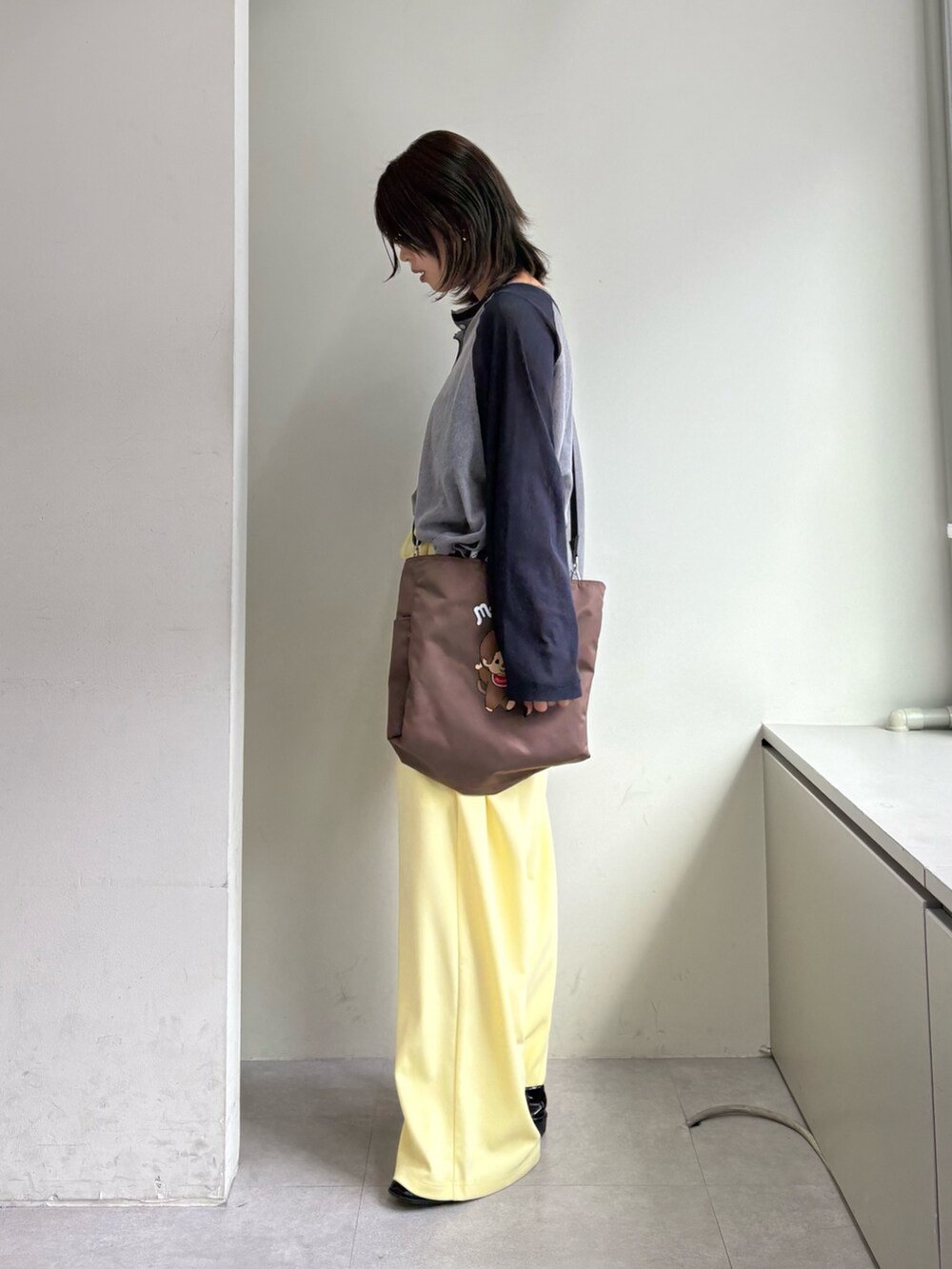 グレー系のTシャツ/カットソー、イエロー系のスラックス、ブラウン系のショルダーバッグを着用したレディースの春コーディネートの2枚目の写真