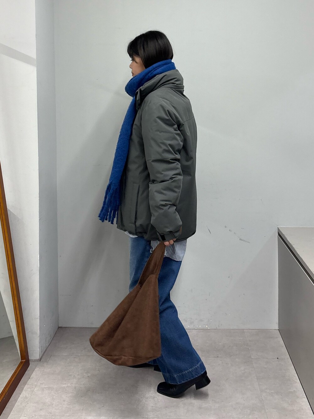 グレー系のダウンジャケット/コート、ブラック系のブーツ、ブルー系のデニムパンツを着用したレディースの冬コーディネートの2枚目の写真