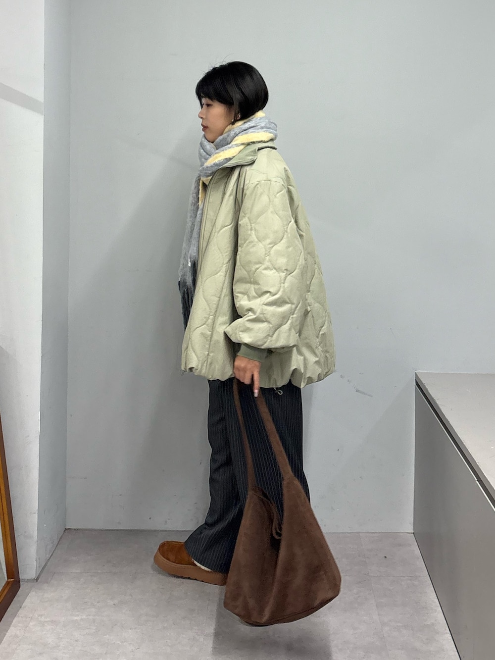 グリーン系のブルゾン、グレー系のスラックス、ブラウン系のトートバッグを着用したレディースの冬コーディネートの2枚目の写真