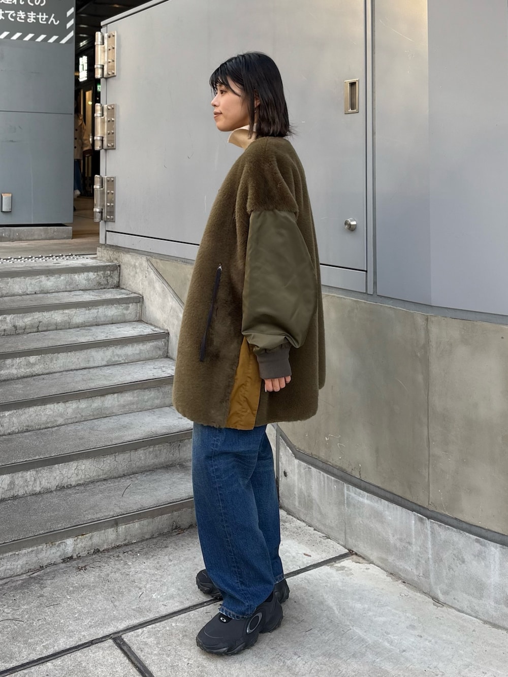 グリーン系のブルゾン、ホワイト系のニット/セーター、ブルー系のデニムパンツを着用したレディースの冬コーディネートの2枚目の写真