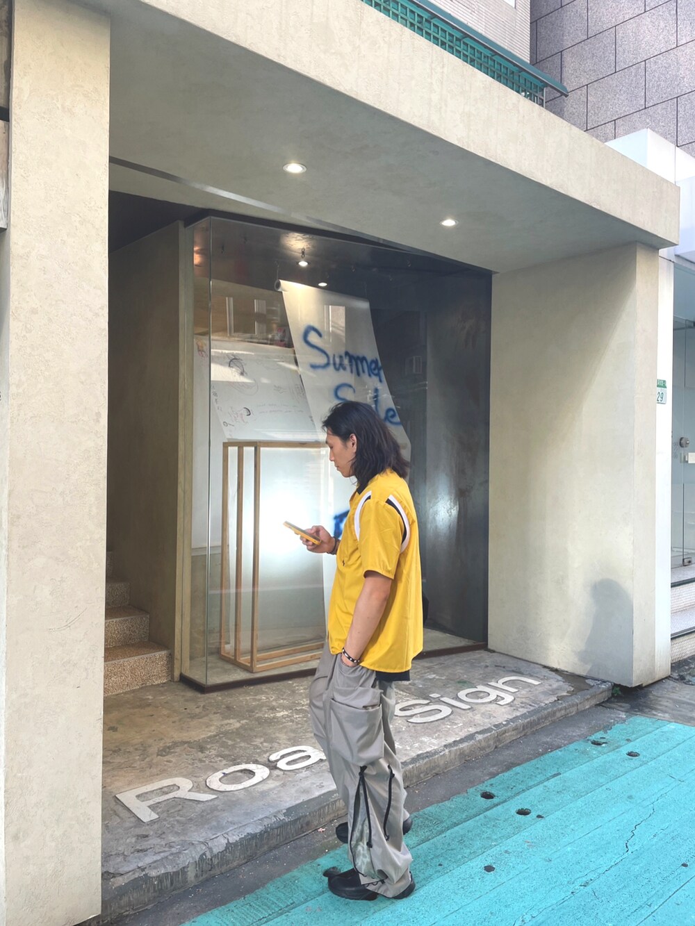 グレー系のチノパンツ、ブラック系のスニーカー、ブラック系のショルダーバッグを着用したメンズの夏コーディネートの2枚目の写真