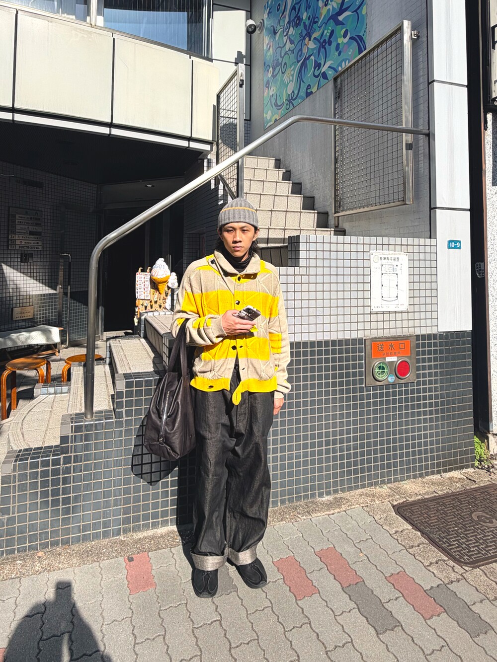 イエロー系のニット/セーター、ブラック系のデニムパンツ、ブラック系のスニーカーを着用したメンズの秋コーディネートの2枚目の写真