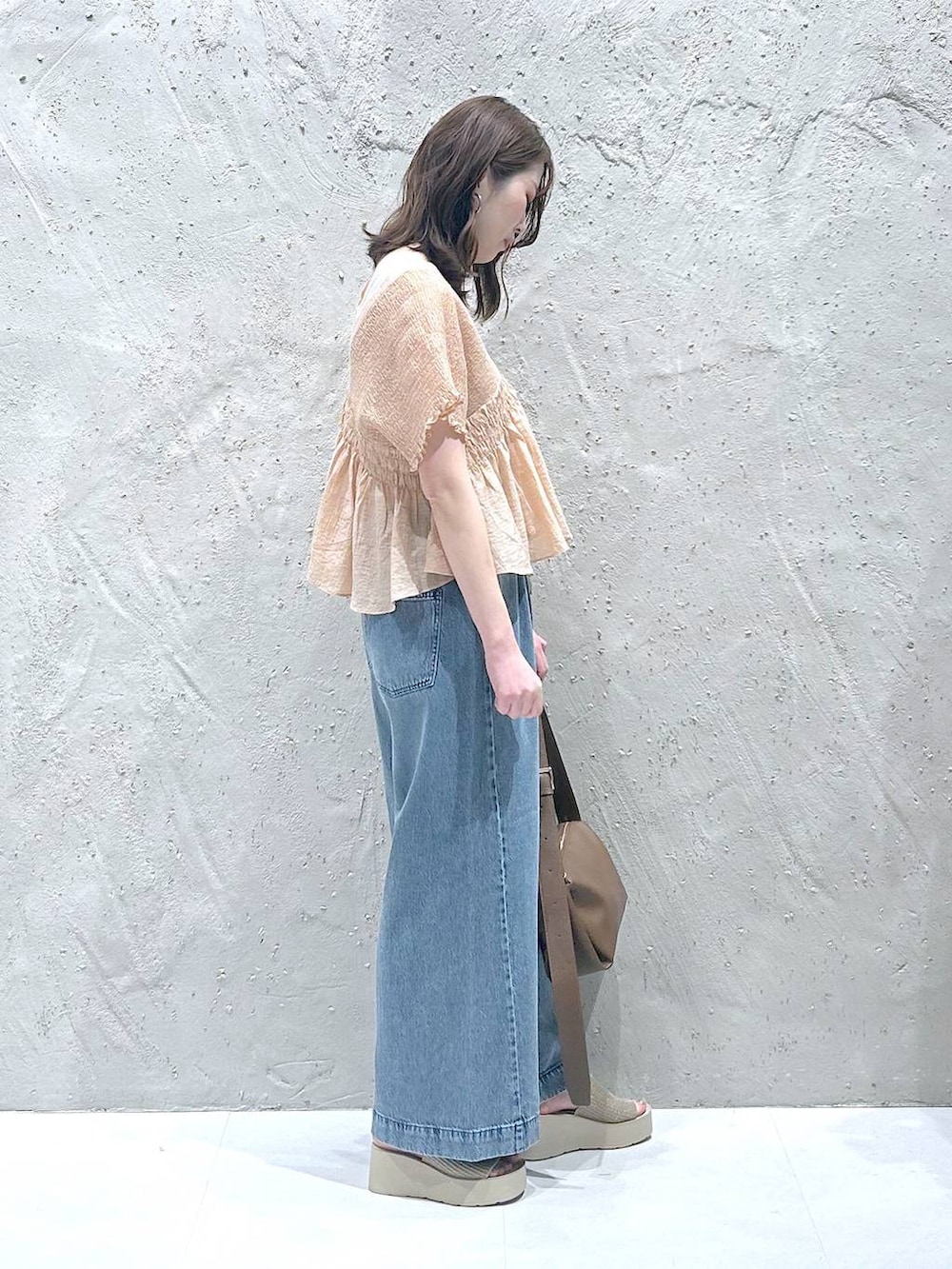 ブルー系のデニムパンツ、ホワイト系のサンダル、ブラウン系のショルダーバッグを着用したレディースの夏コーディネートの2枚目の写真