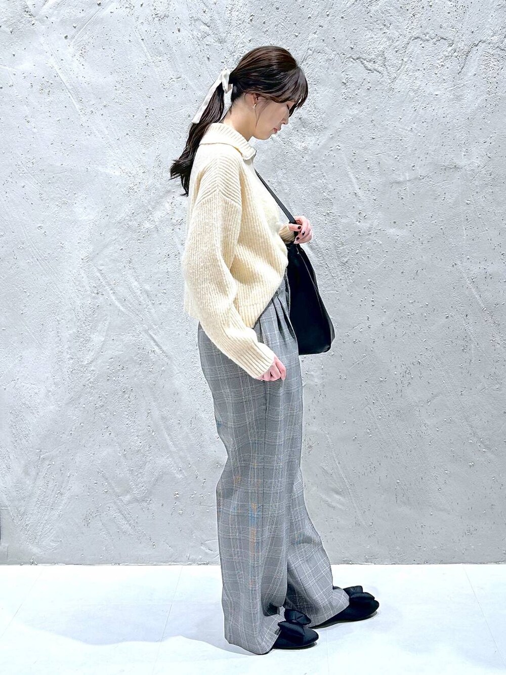 ブラック系のショルダーバッグ、グレー系のスラックス、ホワイト系のニット/セーターを着用したレディースの冬コーディネートの2枚目の写真