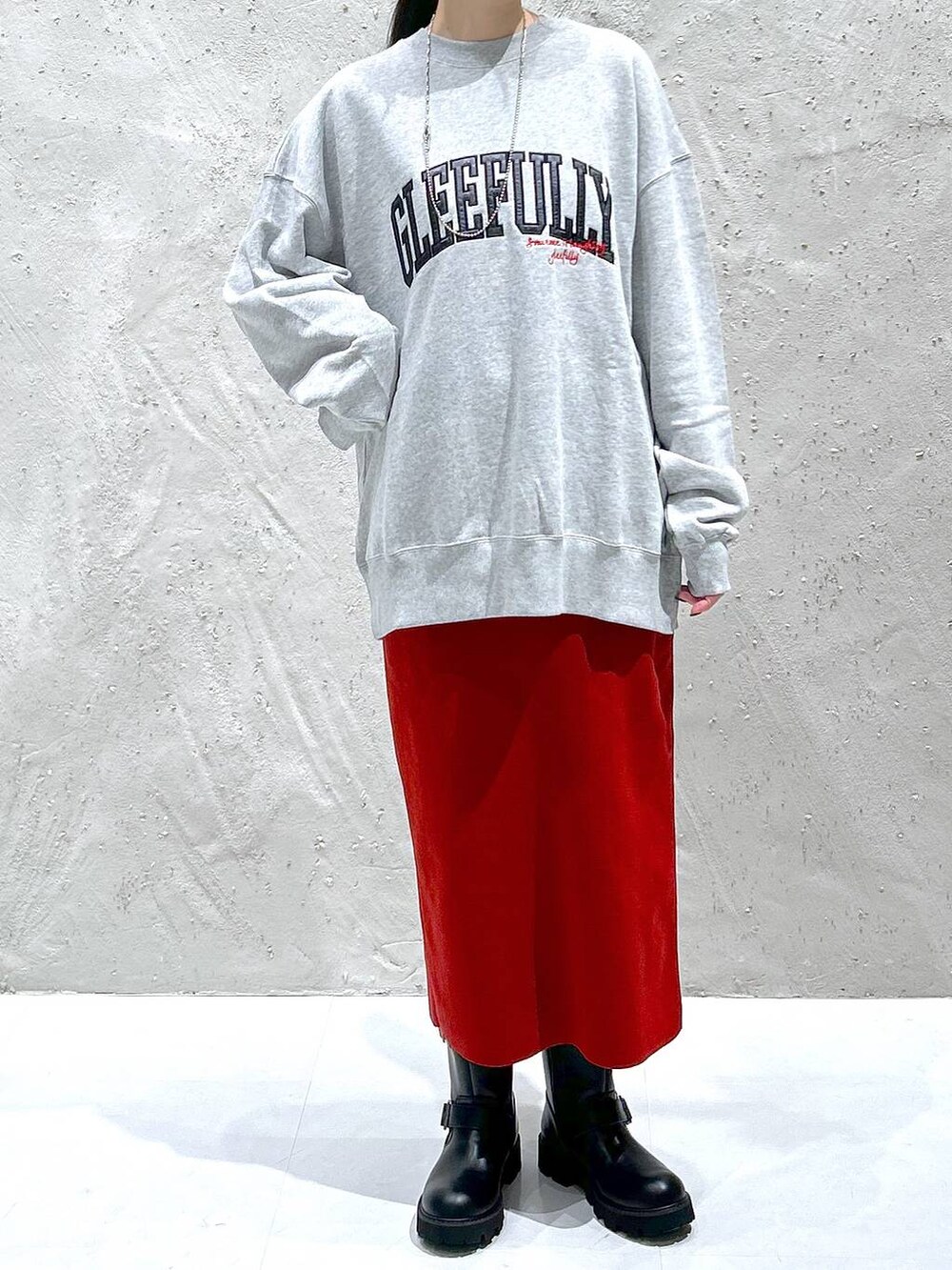 レッド系のスカート、ブラック系のブーツ、グレー系のスウェットを着用したレディースの秋コーディネートの2枚目の写真