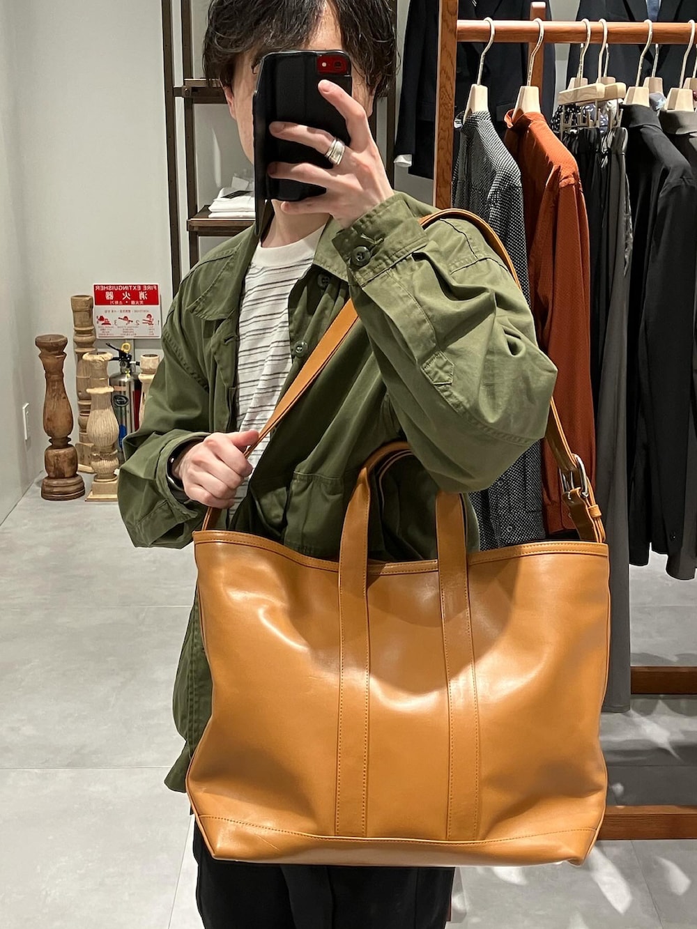 グリーン系のミリタリージャケット、ホワイト系のTシャツ/カットソー、ブラウン系のトートバッグを着用したメンズの春コーディネートの2枚目の写真