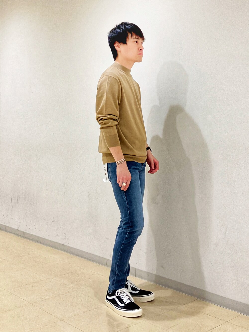 ベージュ系のニット/セーター、ブラック系のスニーカー、ブルー系のデニムパンツを着用したメンズの秋コーディネートの2枚目の写真