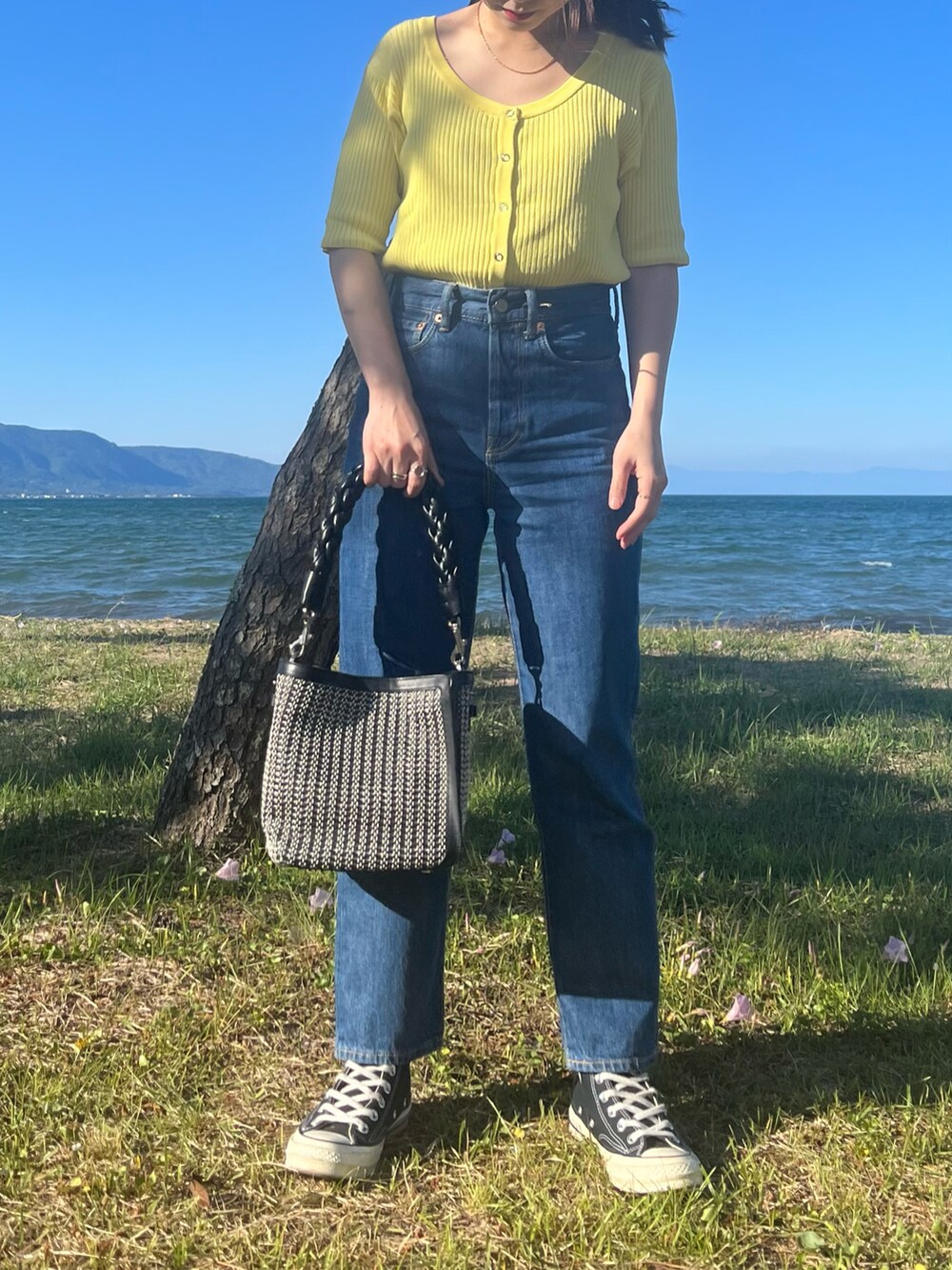 ブラック系のショルダーバッグ、ブラック系のスニーカー、ブルー系のデニムパンツを着用したレディースの春コーディネートの2枚目の写真