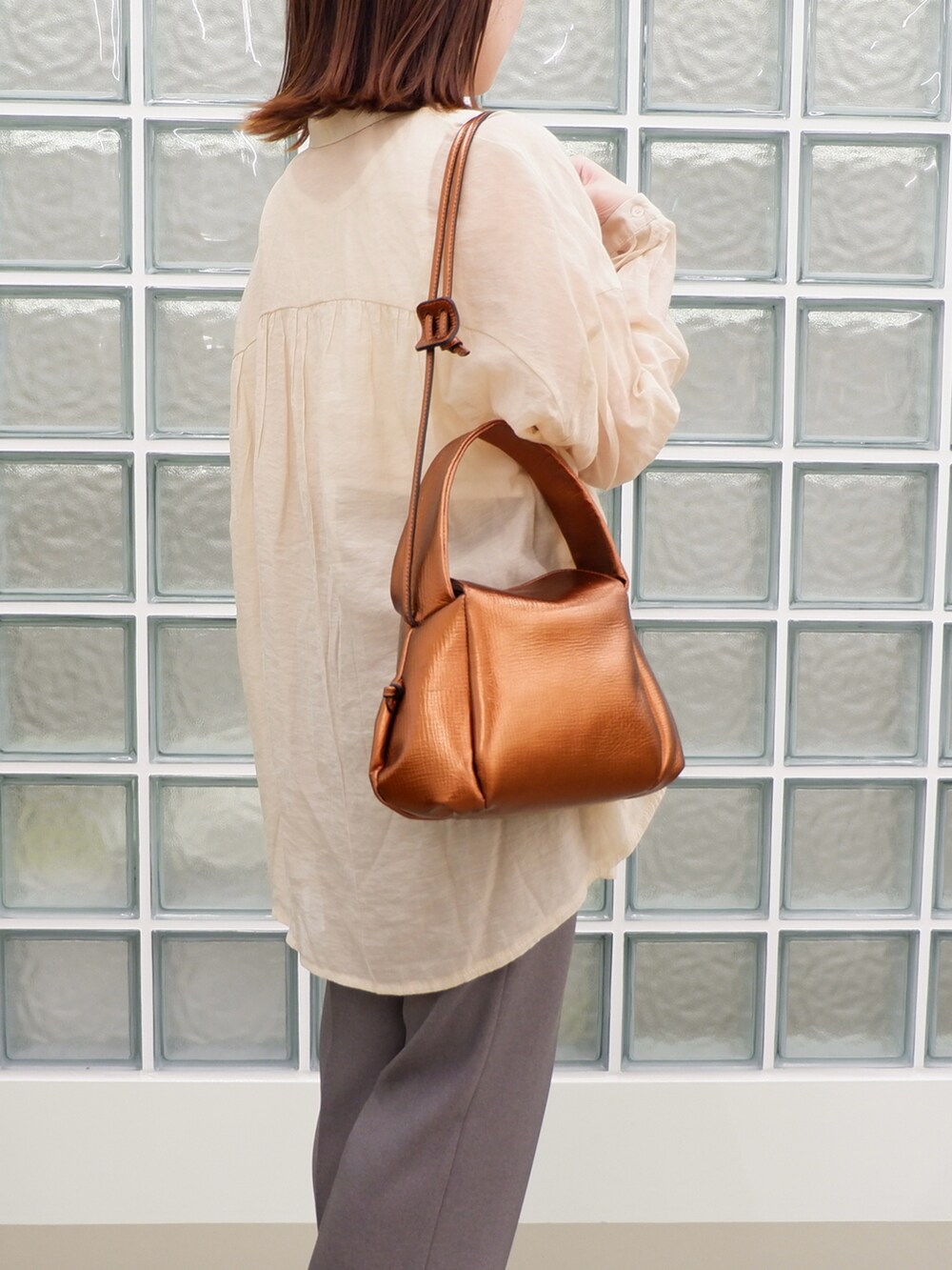 グレー系のスラックス、ブラウン系のバッグ、ベージュ系のシャツ/ブラウスを着用したレディースの春コーディネートの2枚目の写真