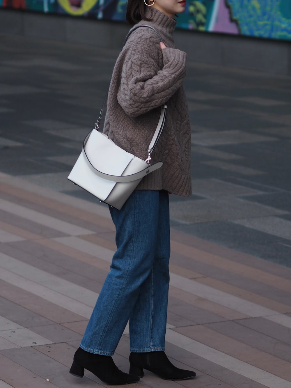 ブルー系のデニムパンツ、ブラック系のブーツ、グレー系のショルダーバッグを着用したレディースの冬コーディネートの2枚目の写真