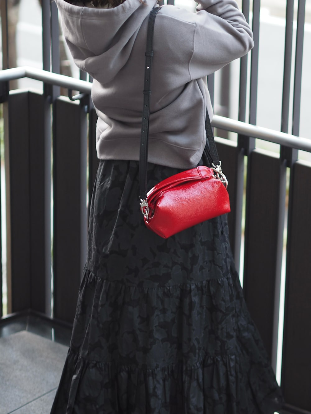 レッド系のクラッチバッグ、ブラック系のスカート、グレー系のスウェットを着用したレディースの冬コーディネートの3枚目の写真