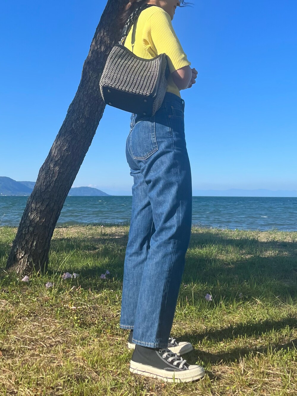 ブラック系のショルダーバッグ、ブラック系のスニーカー、ブルー系のデニムパンツを着用したレディースの春コーディネートの3枚目の写真