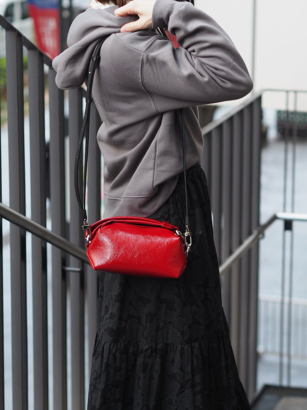 レッド系のクラッチバッグ、ブラック系のスカート、グレー系のスウェットを着用したレディースの冬コーディネートの4枚目の写真