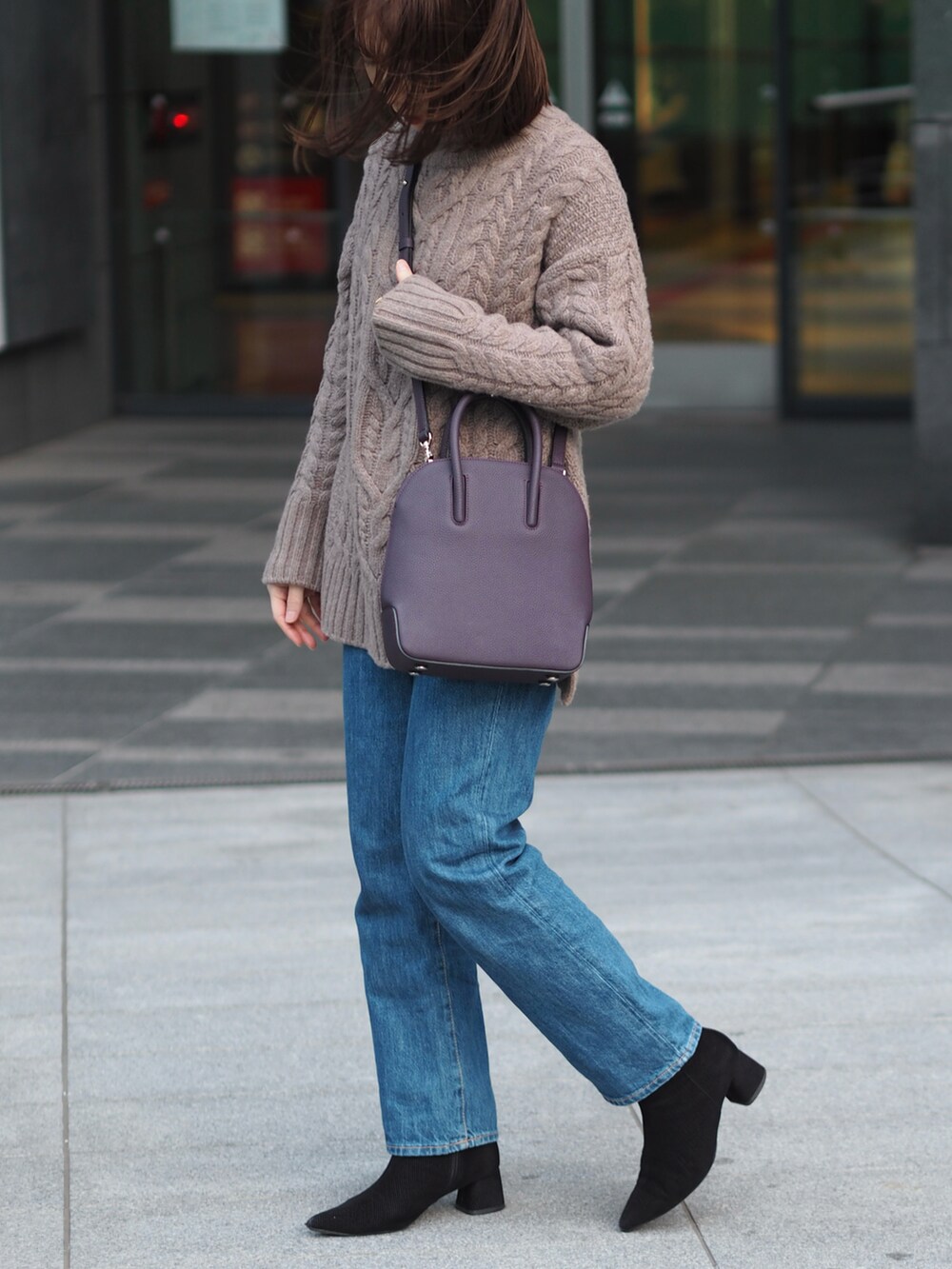 パープル系のバッグ、ブラウン系のニット/セーター、ブルー系のデニムパンツを着用したレディースの冬コーディネートの3枚目の写真