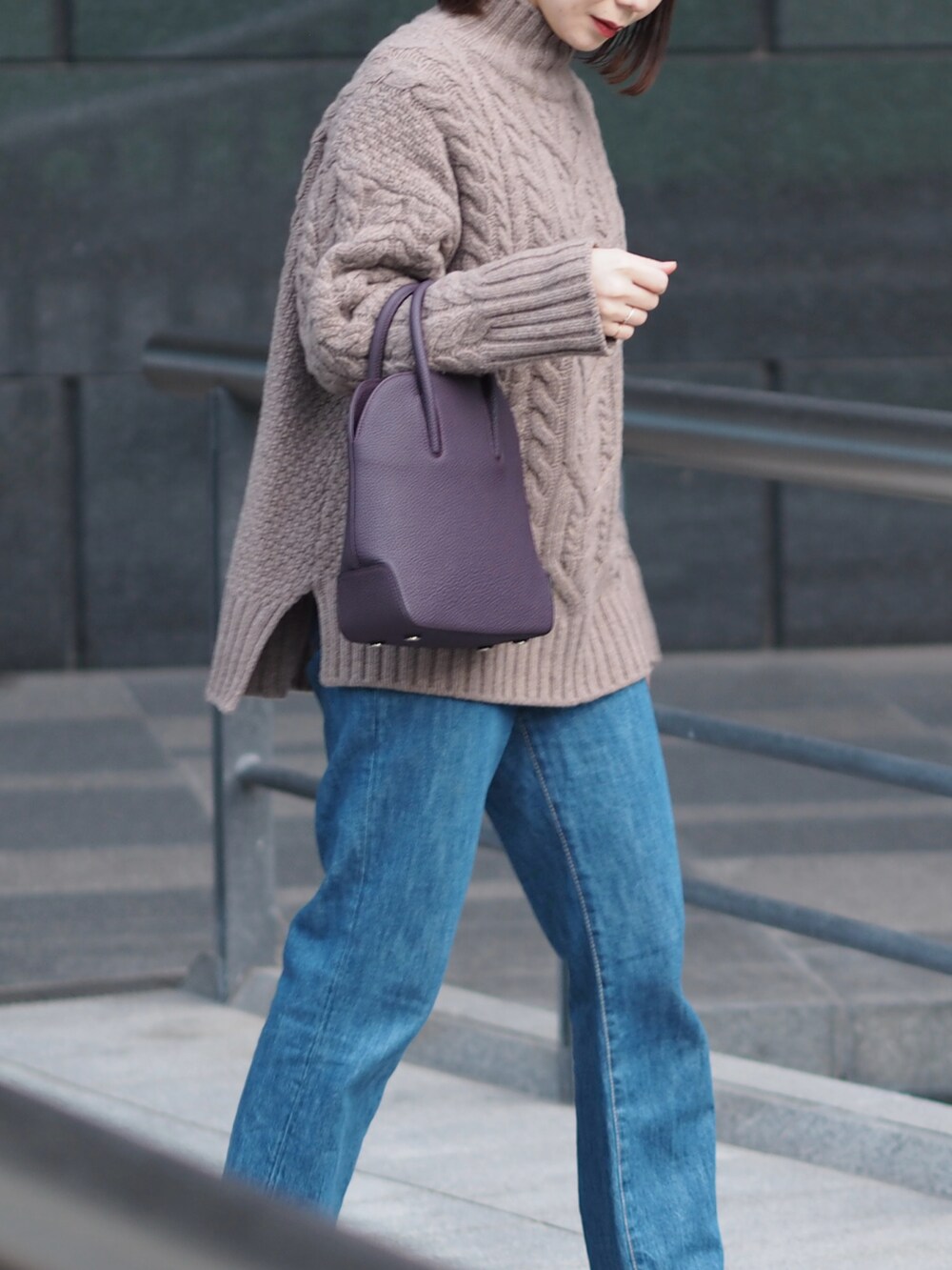 パープル系のバッグ、ブラウン系のニット/セーター、ブルー系のデニムパンツを着用したレディースの冬コーディネートの2枚目の写真