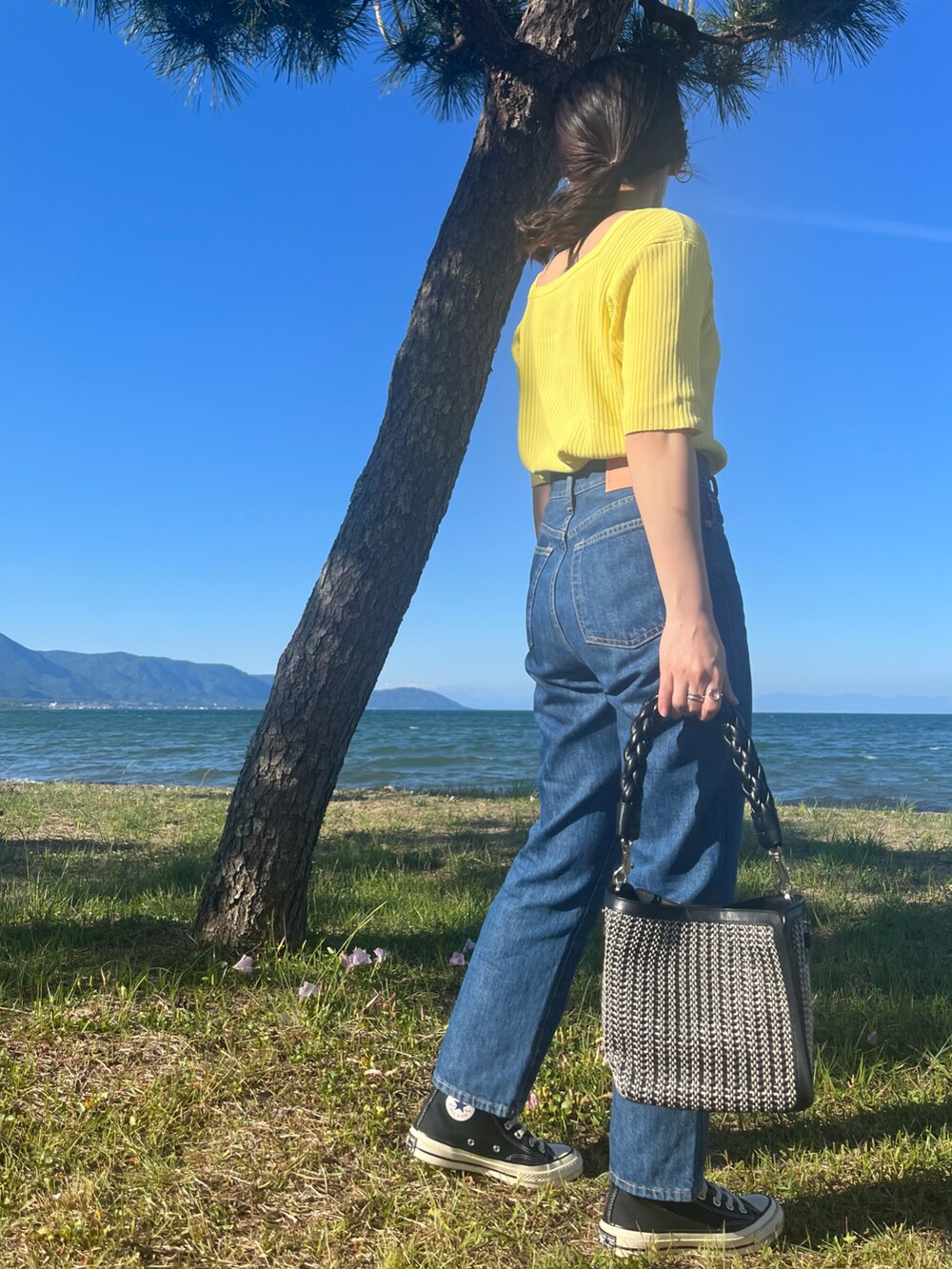 ブラック系のショルダーバッグ、ブラック系のスニーカー、ブルー系のデニムパンツを着用したレディースの春コーディネートの4枚目の写真