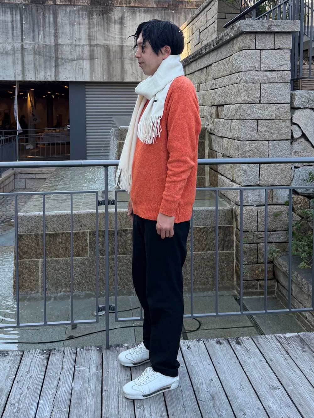 オレンジ系のニット/セーター、ホワイト系のスニーカー、ホワイト系のマフラーを着用したメンズの冬コーディネートの2枚目の写真
