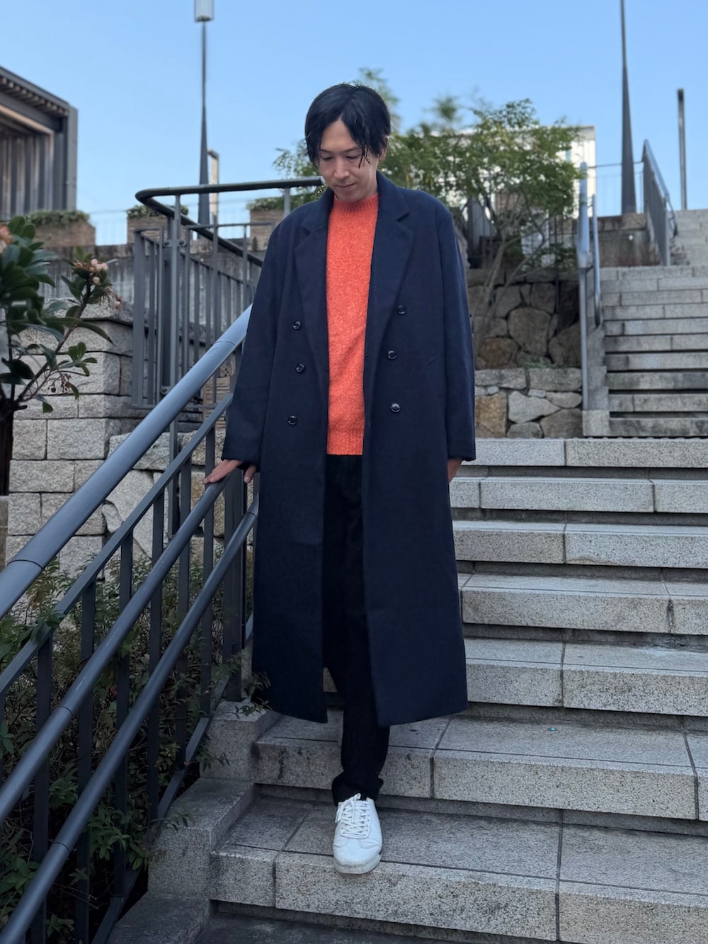 ブルー系のチェスターコート、オレンジ系のニット/セーター、ホワイト系のスニーカーを着用したメンズの冬コーディネートの3枚目の写真