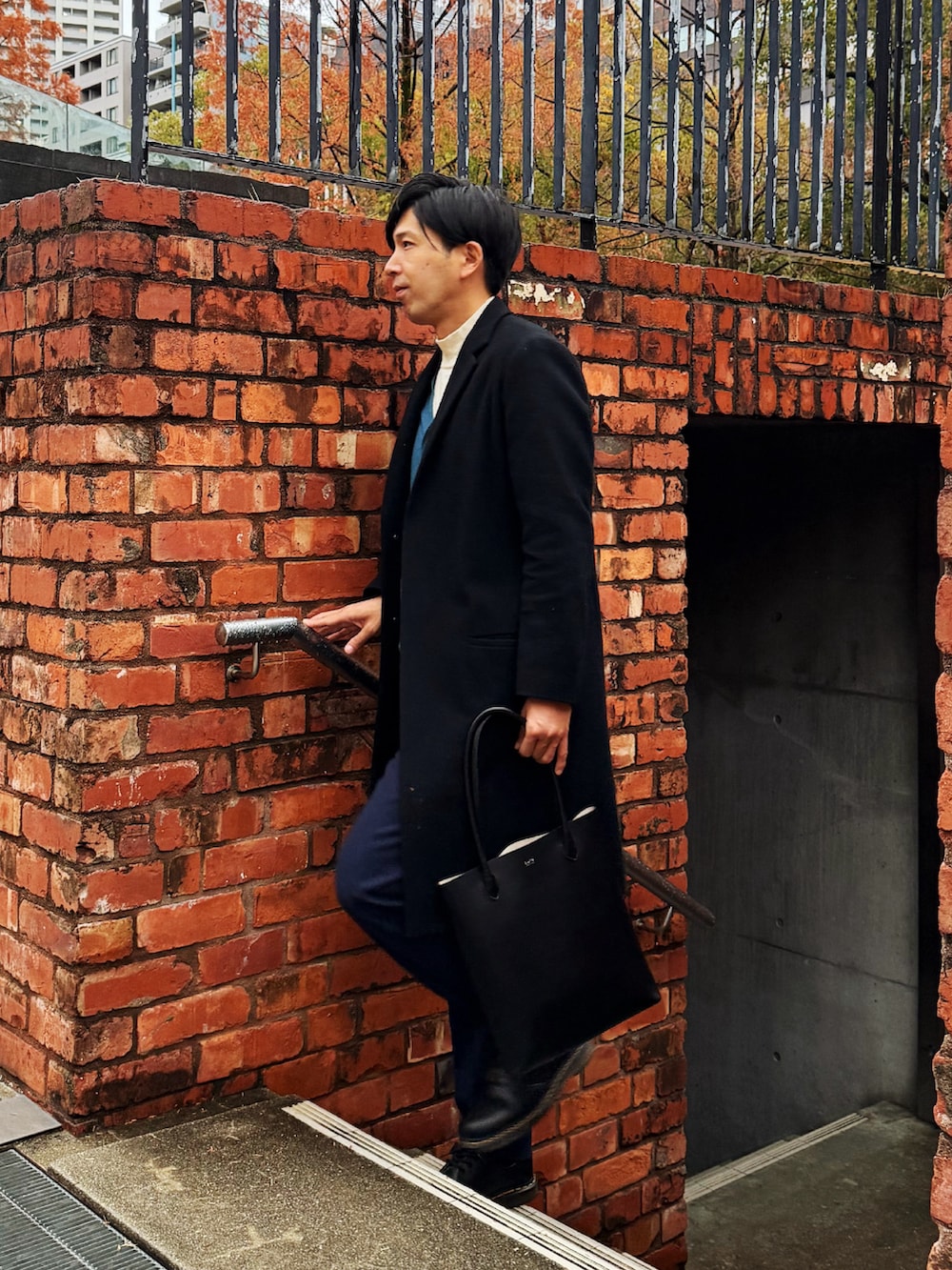 ブラック系のチェスターコート、ブルー系のカーディガン/ボレロ、ホワイト系のニット/セーターを着用したメンズの冬コーディネートの3枚目の写真