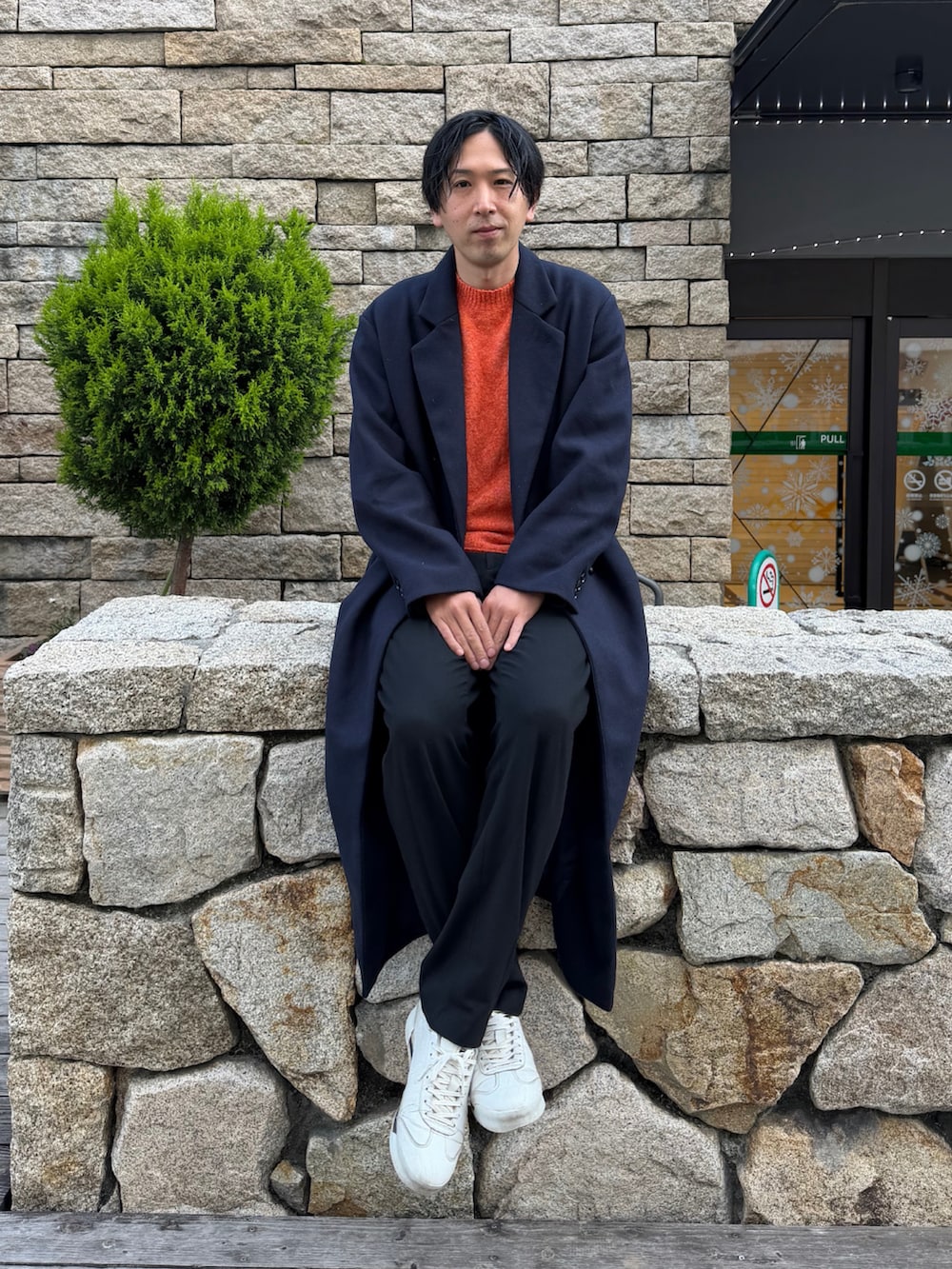 ブルー系のチェスターコート、オレンジ系のニット/セーター、ホワイト系のスニーカーを着用したメンズの冬コーディネートの2枚目の写真