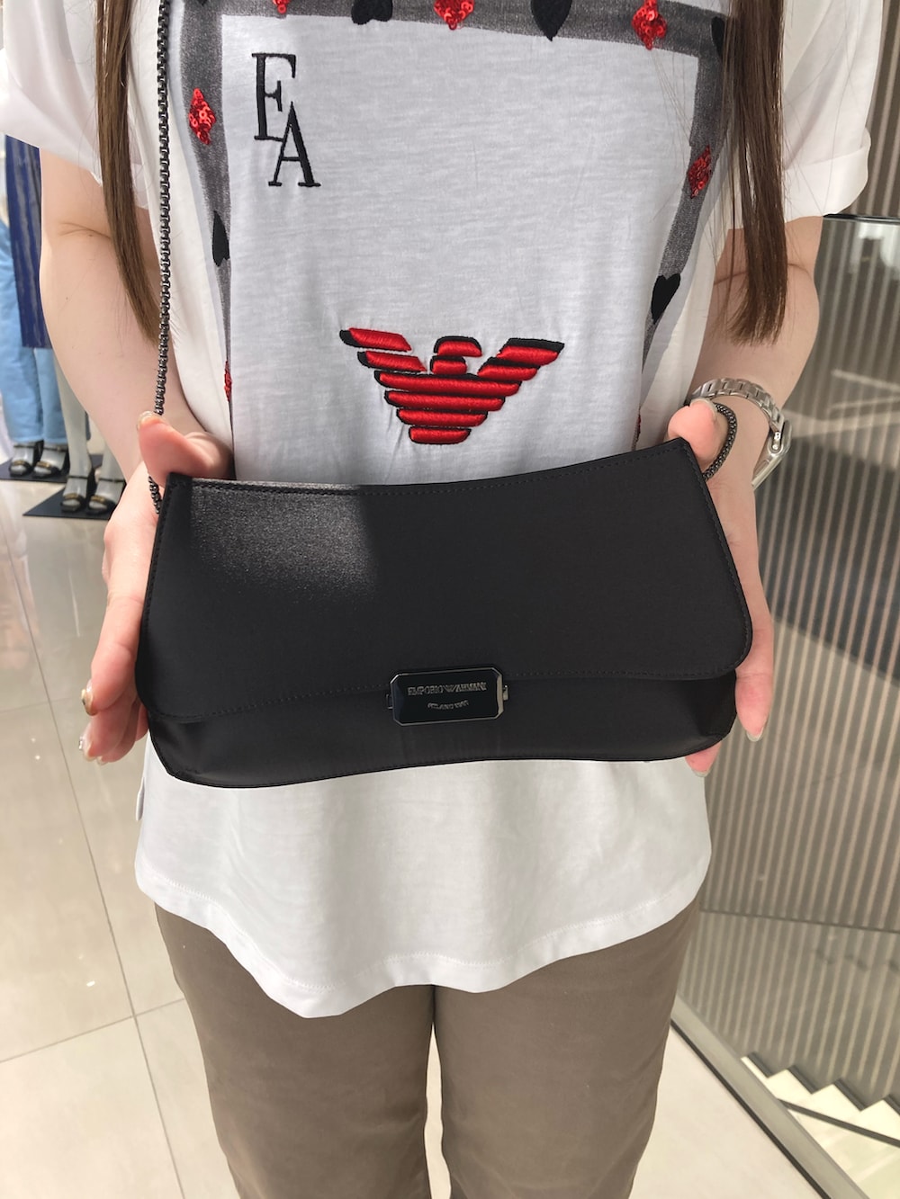 ホワイト系のTシャツ/カットソー、ブラック系のクラッチバッグ、ベージュ系のデニムパンツを着用したレディースの夏コーディネートの2枚目の写真