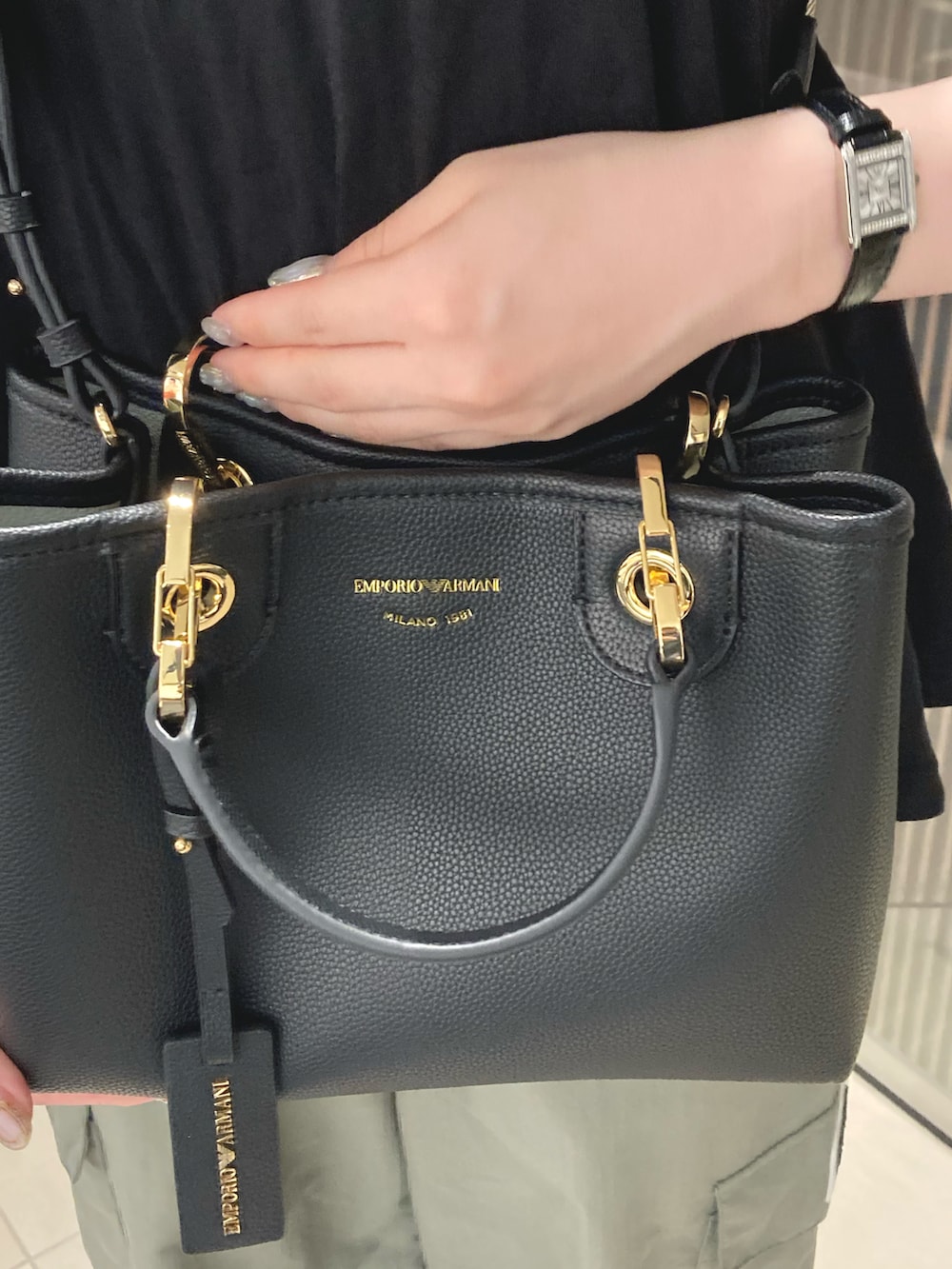 ブラック系のハンドバッグ、グリーン系のカーゴパンツ、ブラック系のアナログ腕時計を着用したレディースの夏コーディネートの2枚目の写真