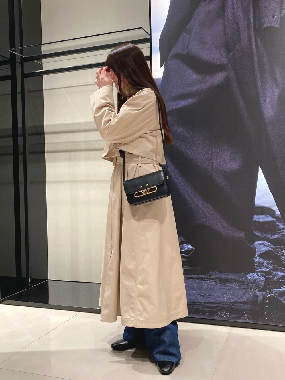 ベージュ系のトレンチコート、ブルー系のデニムパンツ、ブラック系のショルダーバッグを着用したレディースの冬コーディネートの2枚目の写真