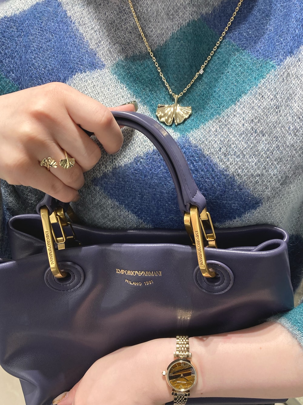 ブルー系のハンドバッグ、ブルー系のスカート、ゴールド系のネックレスを着用したレディースの秋コーディネートの2枚目の写真