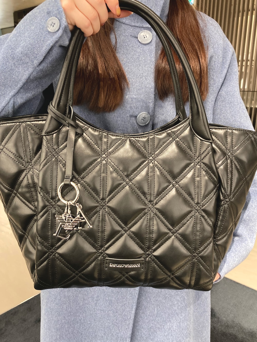 ブルー系のチェスターコート、ブラック系のトートバッグ、シルバー系のピアス（両耳用）を着用したレディースの秋コーディネートの2枚目の写真