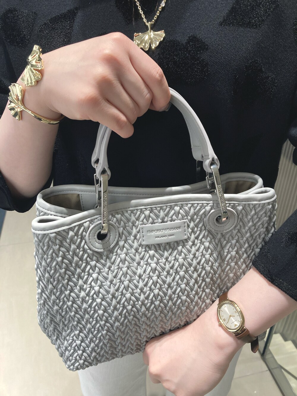 ブラック系のトートバッグ、ゴールド系のネックレス、ブラウン系のアナログ腕時計を着用したレディースの秋コーディネートの2枚目の写真