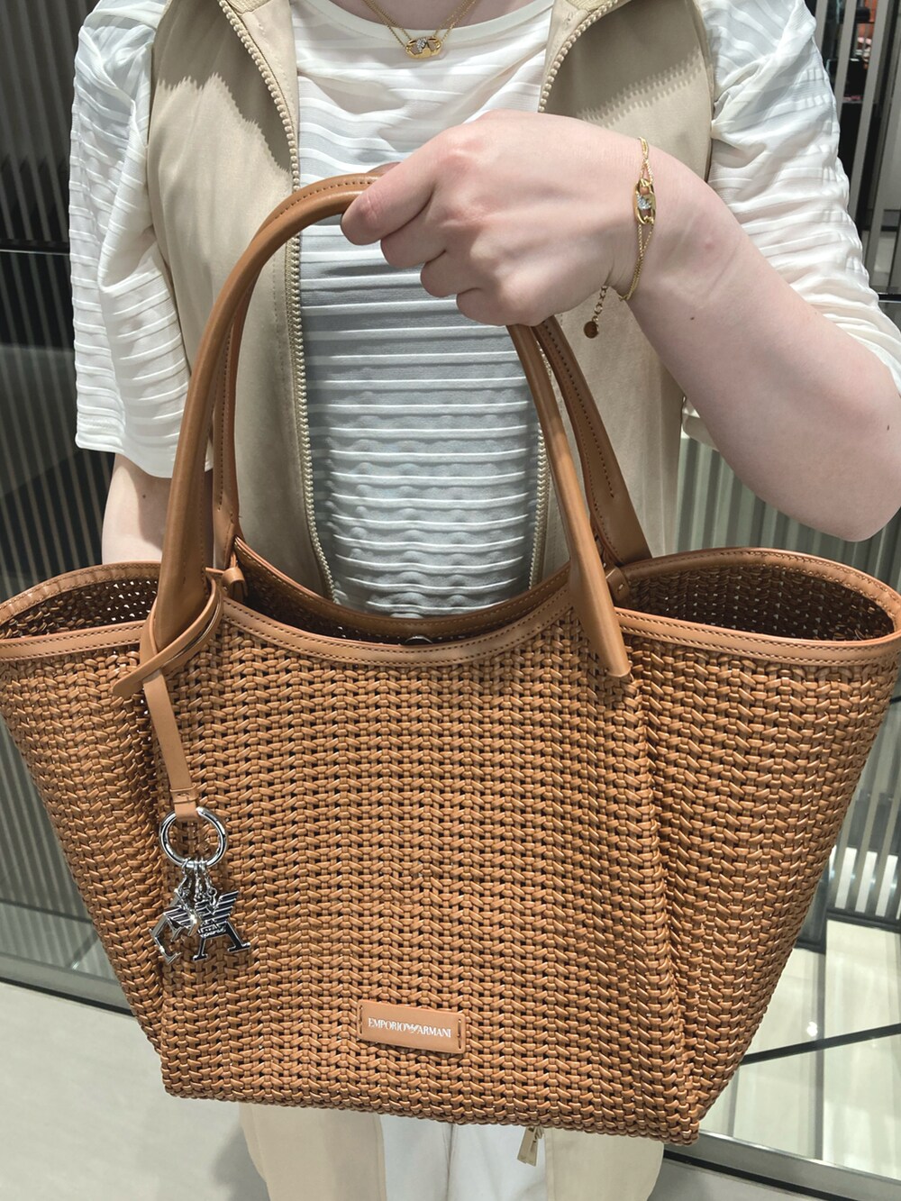 ブラウン系のトートバッグ、ホワイト系のTシャツ/カットソー、ベージュ系のトレンチコートを着用したレディースの春コーディネートの2枚目の写真