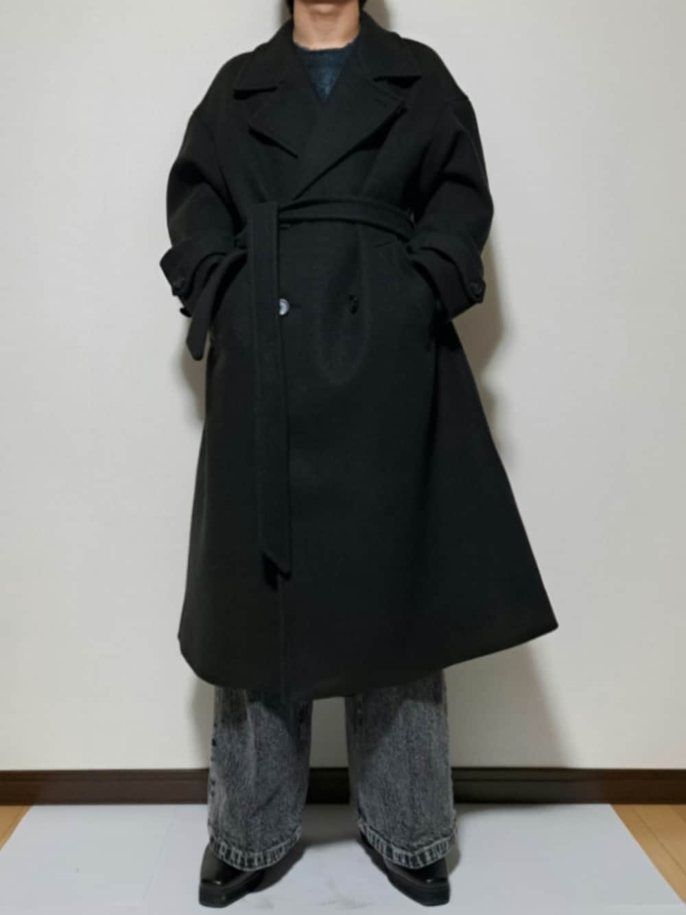 ブラック系のチェスターコート、ブルー系のニット/セーター、ブラック系のブーツを着用したメンズの冬コーディネートの2枚目の写真