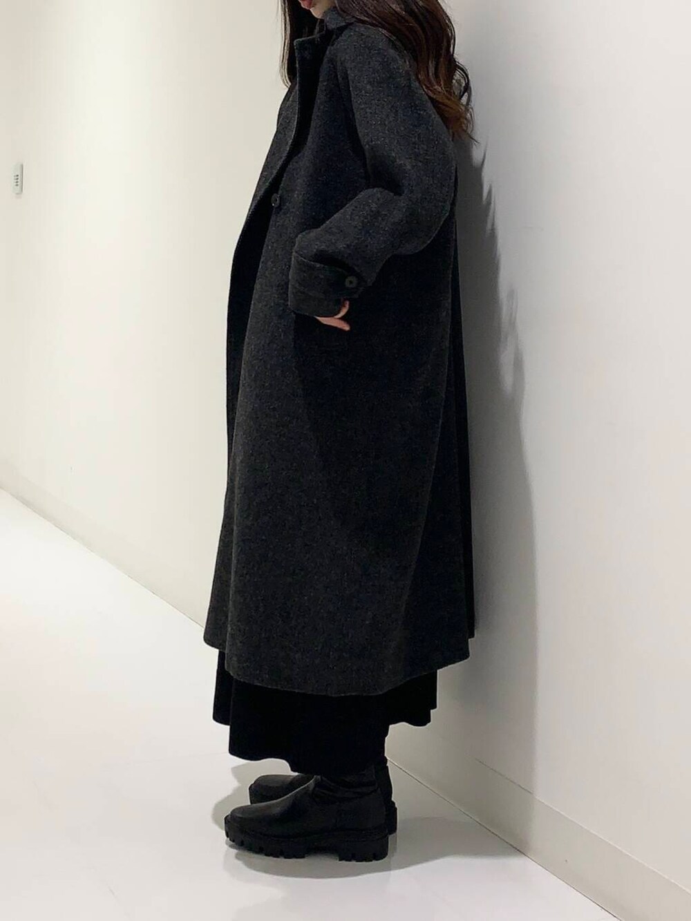 ブラック系のステンカラーコート、ブラック系のブーツ、ブラック系のショルダーバッグを着用したレディースの冬コーディネートの2枚目の写真