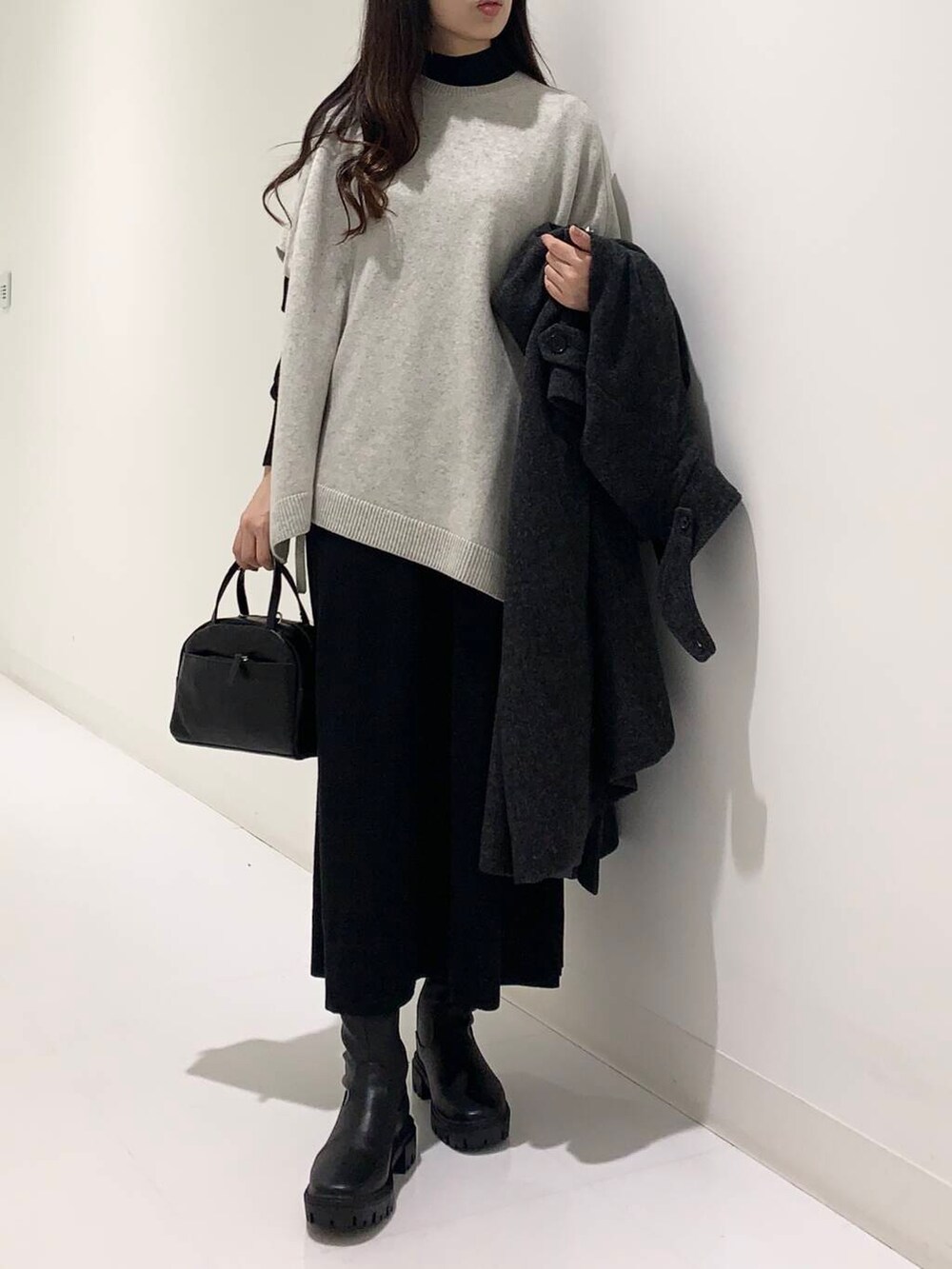 ブラック系のステンカラーコート、ブラック系のブーツ、ブラック系のショルダーバッグを着用したレディースの冬コーディネートの4枚目の写真