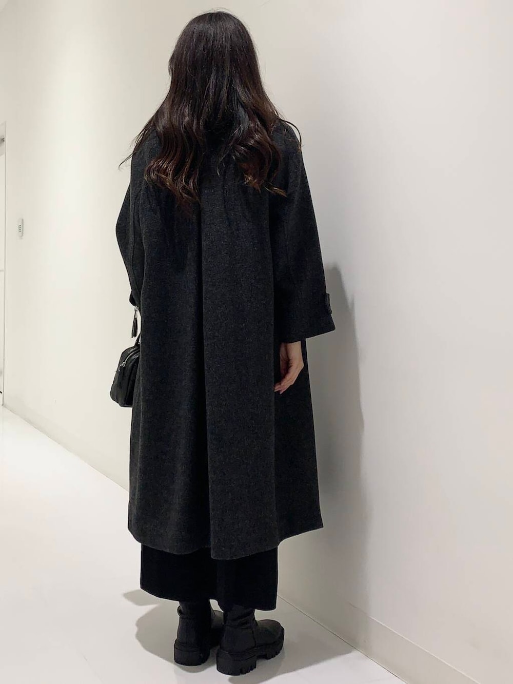 ブラック系のステンカラーコート、ブラック系のブーツ、ブラック系のショルダーバッグを着用したレディースの冬コーディネートの3枚目の写真