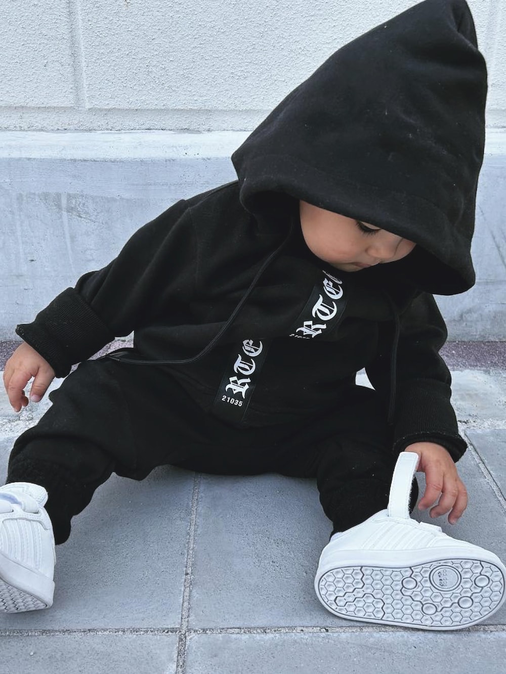 ブラック系のパーカー、ブラック系のスウェットパンツ、ホワイト系のベビーシューズ/ベビーソックスを着用したキッズの春コーディネートの2枚目の写真