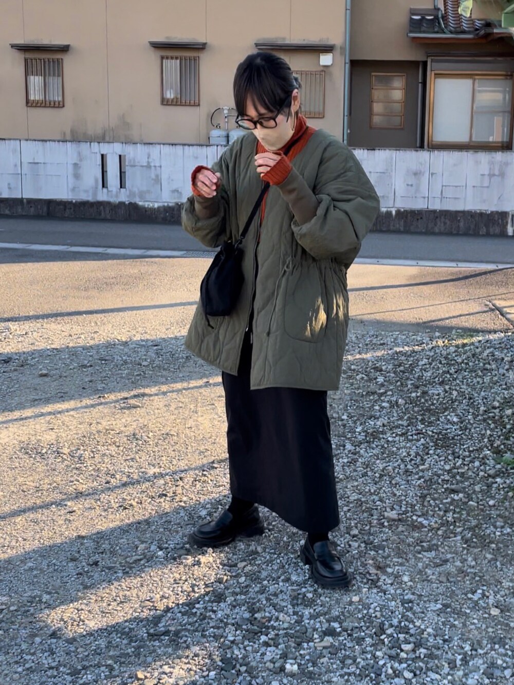 グリーン系のミリタリージャケット、ブラック系のスカート、オレンジ系のニット/セーターを着用したレディースの秋コーディネートの2枚目の写真