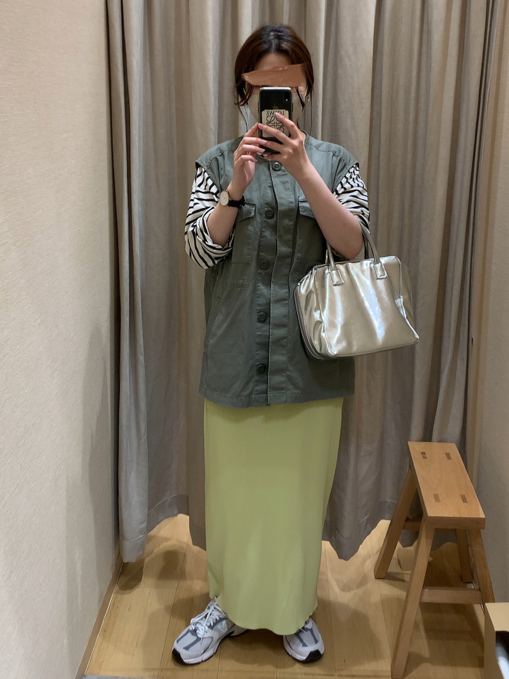グリーン系のベスト、イエロー系のスカート、グレー系のスニーカーを着用したレディースの春コーディネートの2枚目の写真