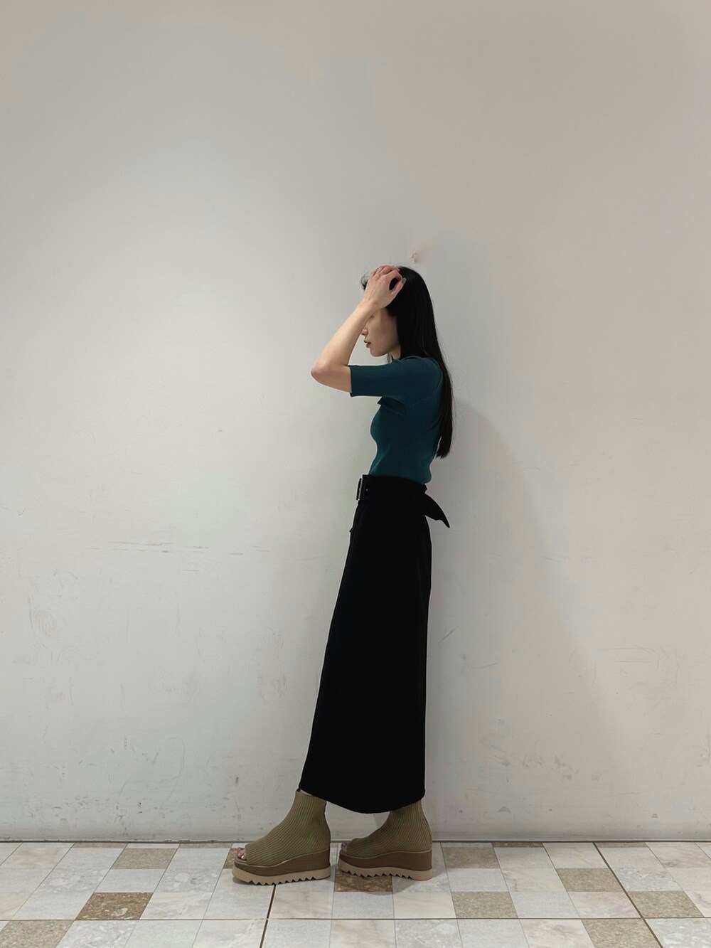 グリーン系のニット/セーター、ブラック系のスカート、ベージュ系のブーツを着用したレディースの春コーディネートの3枚目の写真