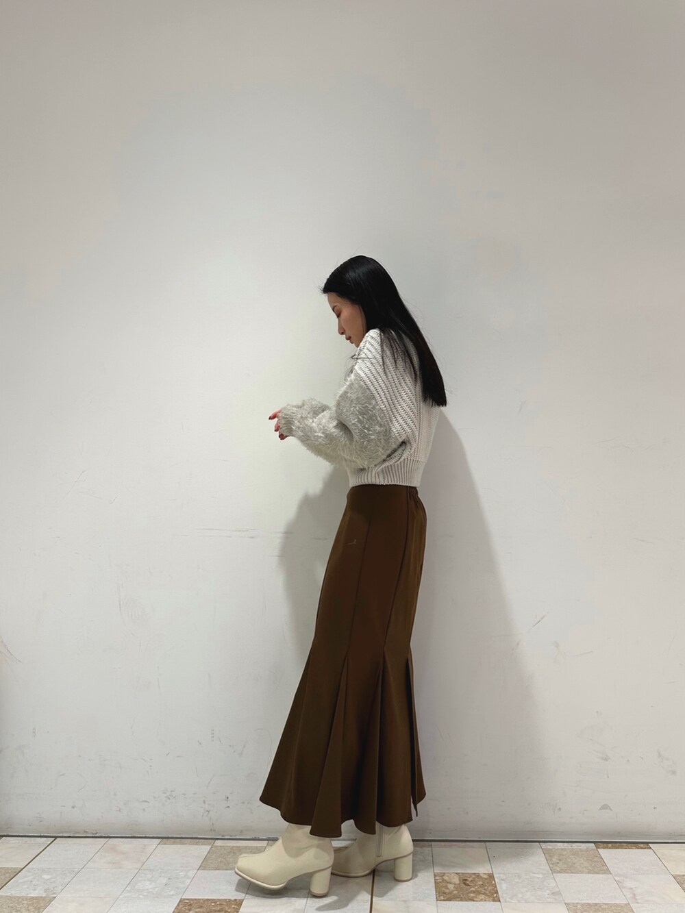 ブラウン系のスカート、グレー系のニット/セーター、ホワイト系のブーツを着用したレディースの冬コーディネートの2枚目の写真