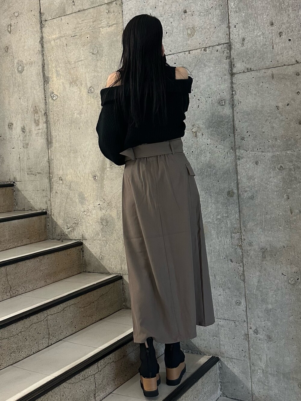 ブラウン系のスカート、ブラック系のニット/セーター、ブラック系のブーツを着用したレディースの冬コーディネートの2枚目の写真