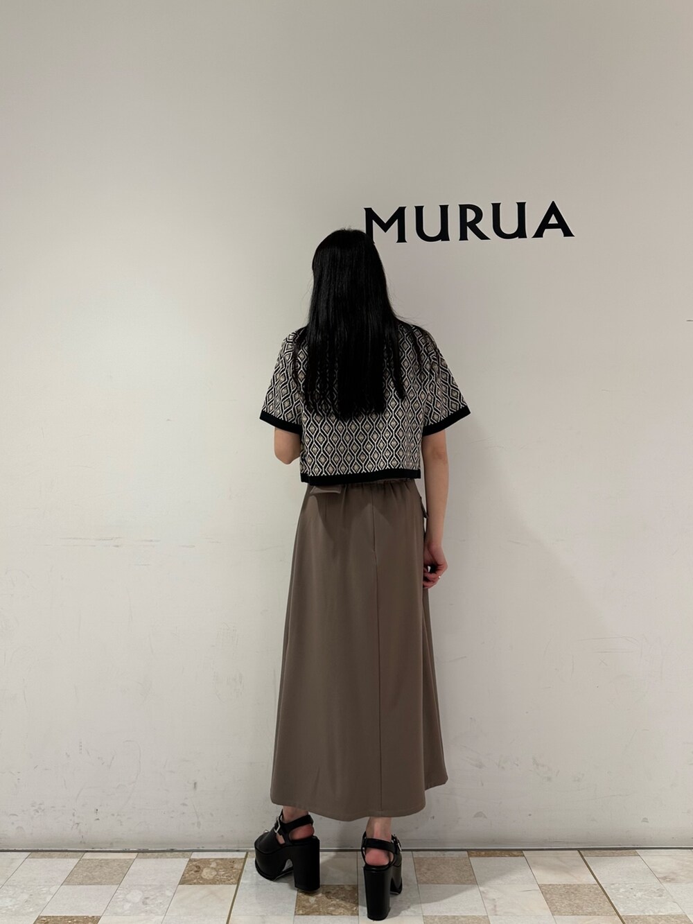 ブラウン系のスカート、ブラック系のポロシャツ、ブラック系のサンダルを着用したレディースの春コーディネートの3枚目の写真