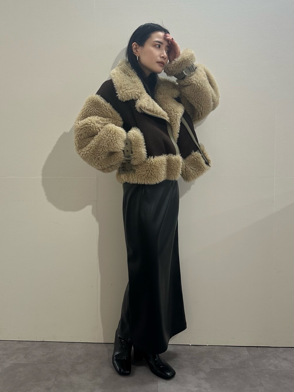 ブラック系のスカート、ブラウン系のムートンコート、レッド系のニット/セーターを着用したレディースの冬コーディネートの2枚目の写真